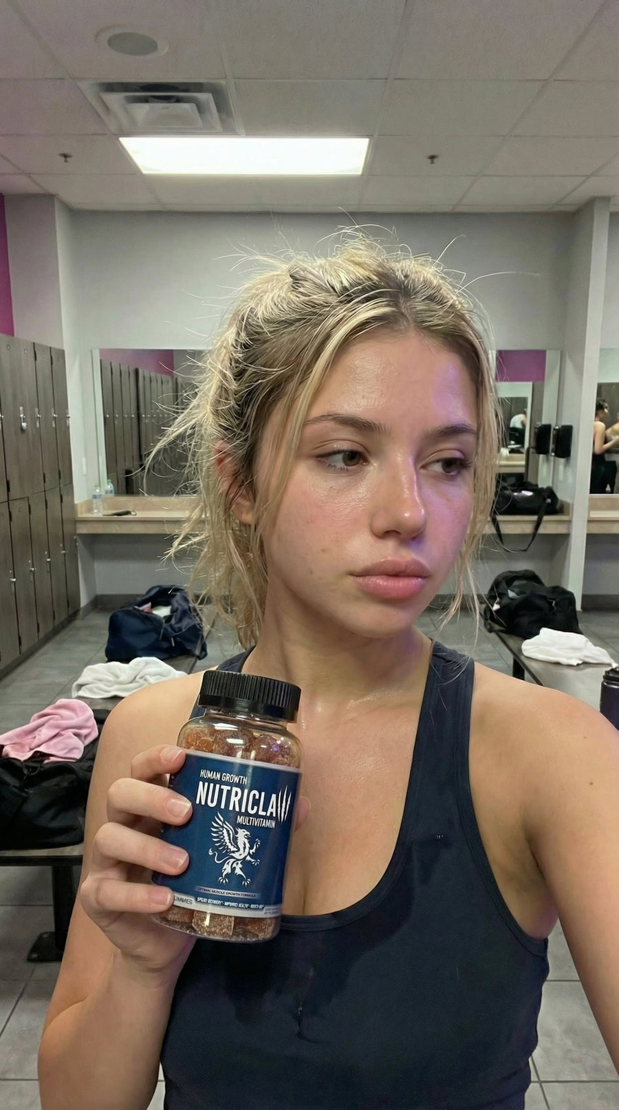 Woman at the gym holding a NutriClaw daily supplement bottle